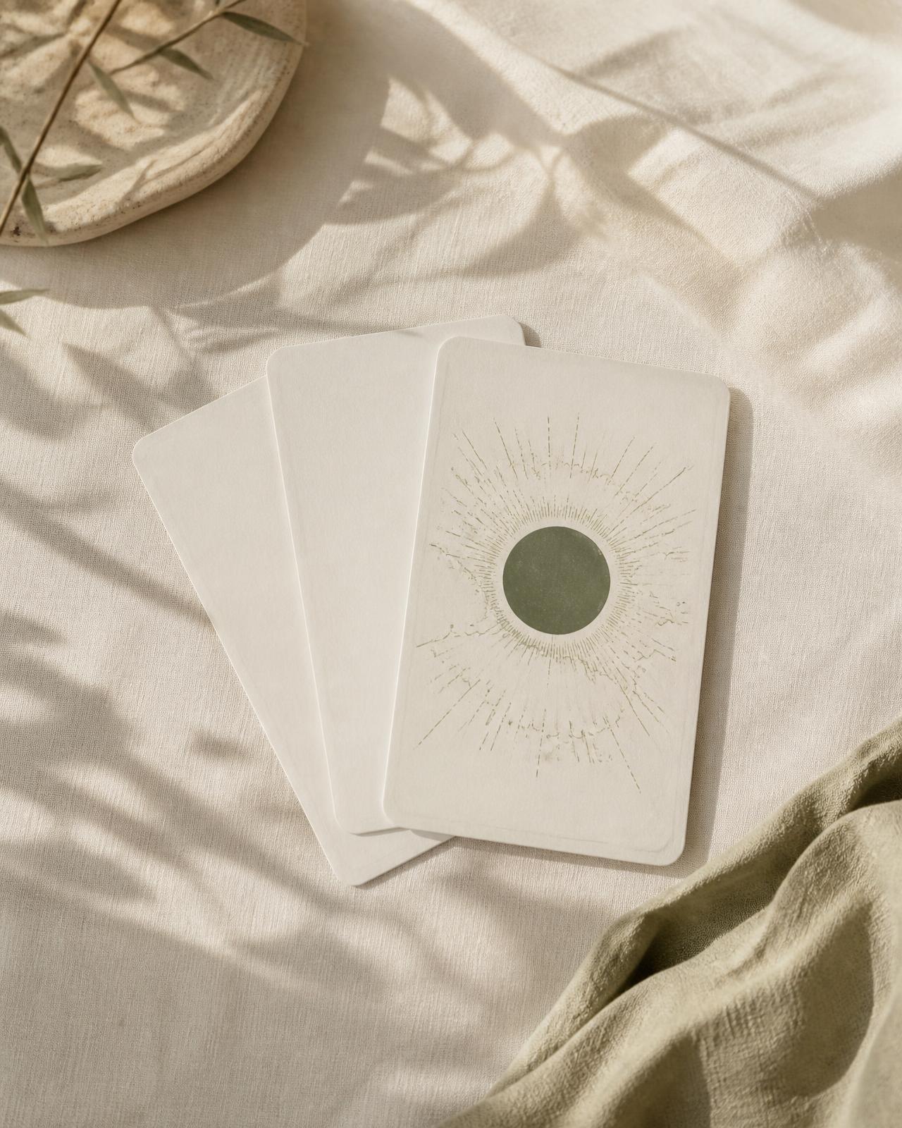Ivory tarot cards fanned on cream linen, the top card marked with a fine eclipse motif